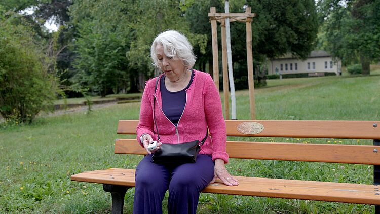 Mobiler Hausnotruf – Sicherheit unterwegs mit dem DRK Mittelhessen Seniorin drückt mobilen Notrufknopf auf einer Parkbank