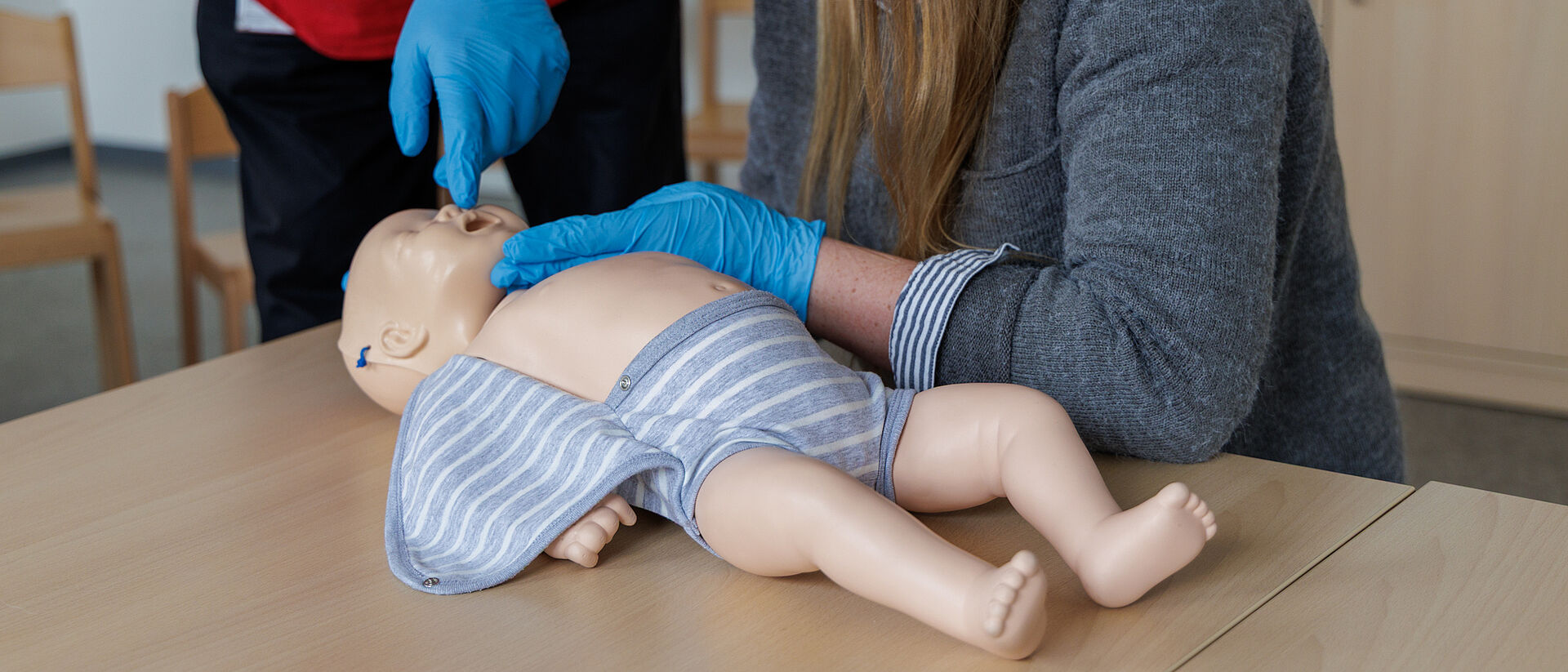 Erste Hilfe am Kind – Atemkontrolle Säugling Teilnehmer prüfen Atmung einer Säuglingspuppe im Erste Hilfe am Kind Kurs