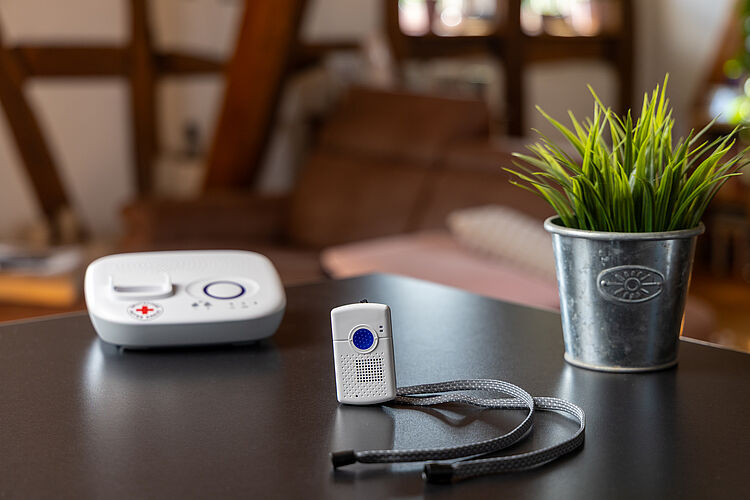 DRK Hausnotruf – zuverlässige Hilfe auf Knopfdruck Hausnotrufgerät mit Notrufsender und rotem Kreuz auf einem Tisch