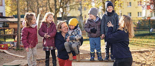Gemeinsam stark – Kinder und Erzieherinnen in der DRK-Kita Mittelhessen Kinder und Erzieherinnen lachen gemeinsam auf dem Spielplatz einer DRK-Kita