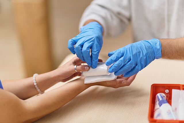 DRK Erste Hilfe: Wundversorgung und Verband anlegen Person mit blauen Handschuhen legt einen Verband an einer Hand an