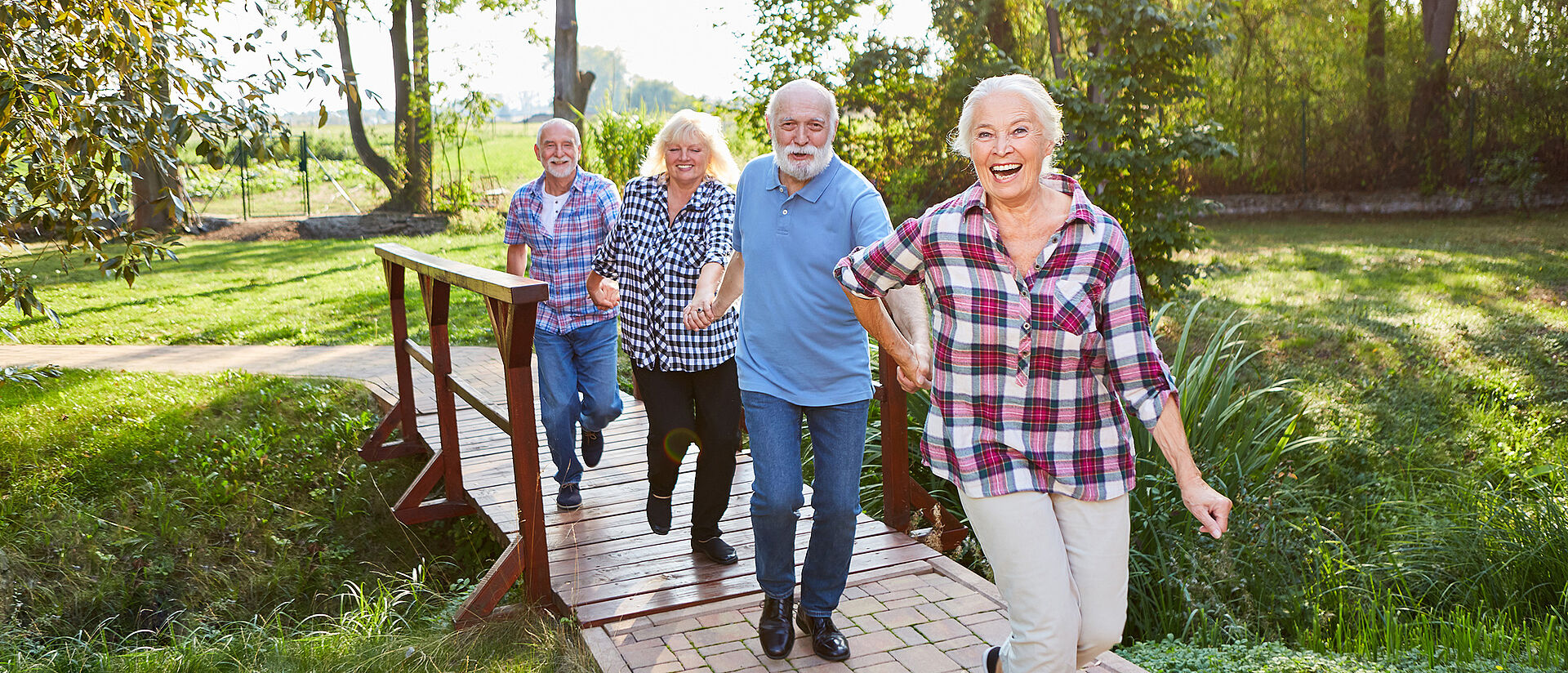 Seniorenangebote beim DRK Mittelhessen – Aktiv, sicher und gut betreut Fröhliche Seniorengruppe beim gemeinsamen Spaziergang über eine Holzbrücke im Grünen