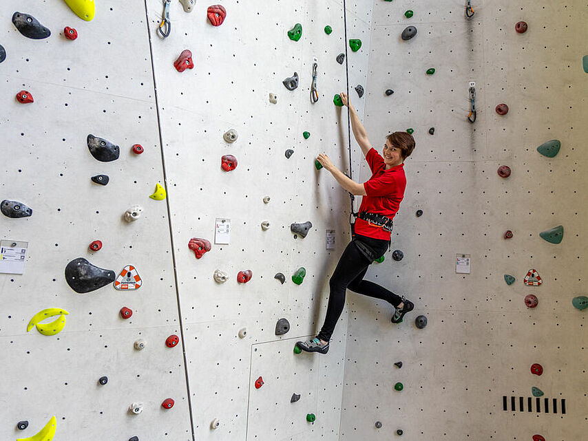 Therapeutisches Klettern beim DRK Mittelhessen – Kraft und Vertrauen aufbauen Frau klettert gesichert an einer hellen Kletterwand während eines therapeutischen Trainings