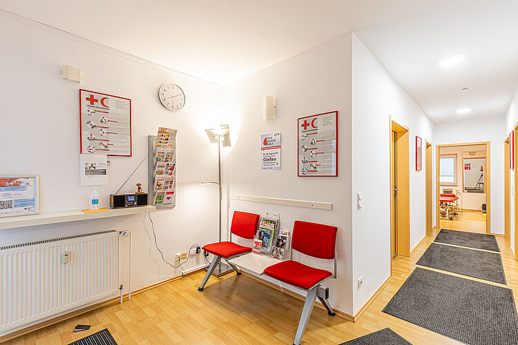 Wartebereich der DRK Therapiepraxis Alten-Buseck Wartebereich mit roten Stühlen und DRK-Informationsmaterial