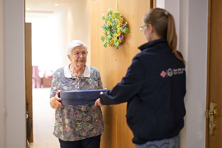Essen auf Rädern – DRK Mittelhessen liefert Mahlzeiten nach Hause DRK-Mitarbeiterin übergibt Seniorin eine Mahlzeit im Rahmen des Angebots Essen auf Rädern