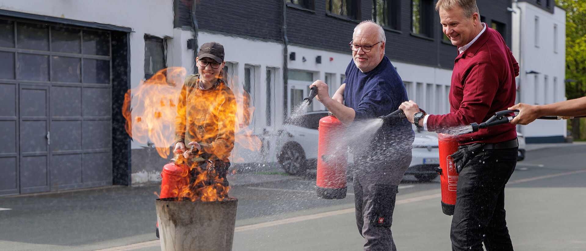Brandschutzhelfer Kurs DRK Mittelhessen Feuerlöschtraining Mehrere Teilnehmer löschen gemeinsam ein Feuer mit Feuerlöschern bei Übung