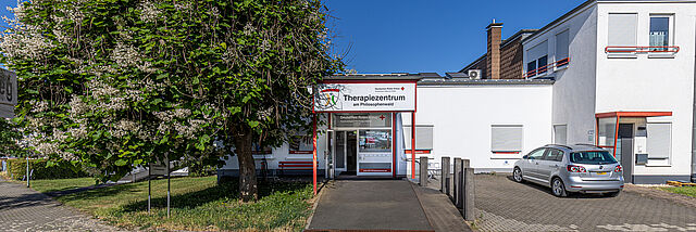 DRK Therapiezentrum am Philosophenwald Gießen – Gesundheitsförderung durch Ergotherapie & Logopädie Eingang des DRK Therapiezentrums am Philosophenwald in Gießen mit Baum, Rampe und geparktem Auto bei sonnigem Wetter