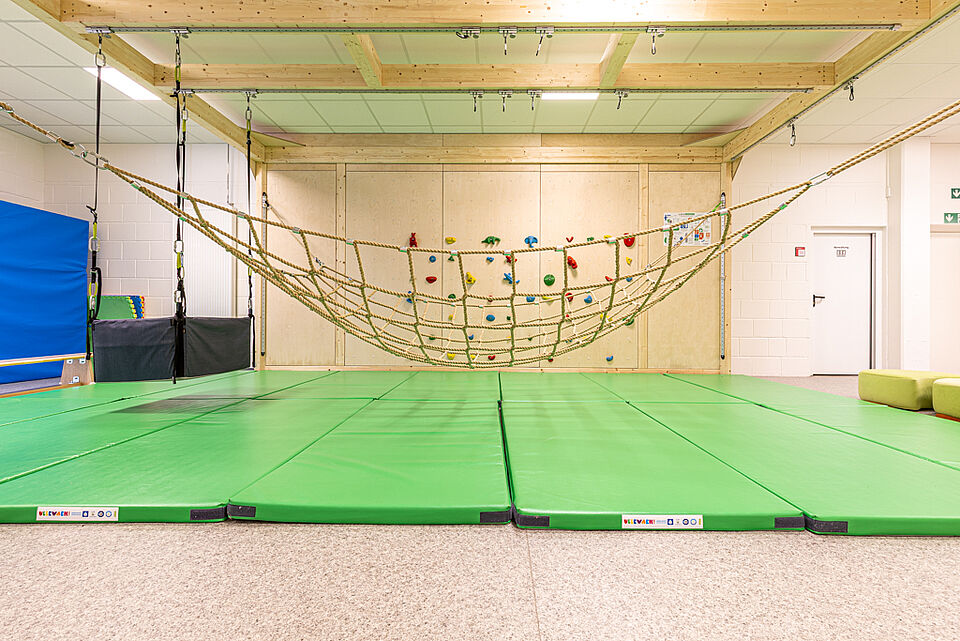 Kletterwand und Bewegungsfläche in der DRK-Kita „Henrys Märchenwelt“ Große grüne Turnfläche mit Kletternetz und bunten Griffen in der DRK-Kita Heuchelheim