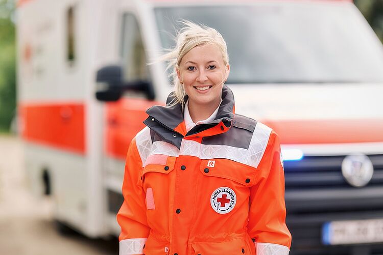Sanitätsdienst beim DRK Mittelhessen – Hilfe, wenn’s drauf ankommt Lächelnde DRK-Notfallsanitäterin steht vor Rettungswagen