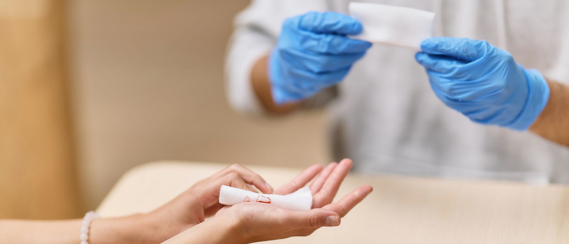 DRK Erste Hilfe: Wundversorgung mit Kompresse Helfende Person mit blauen Handschuhen bereitet eine Kompresse für eine Handverletzung vor