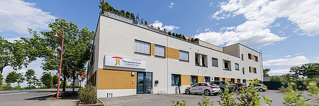 DRK Therapiezentrum in Stadtallendorf – Moderne Einrichtung für Physiotherapie & Ergotherapie Außenansicht des DRK Therapiezentrums in Stadtallendorf mit Parkplatz und Fahrzeugen bei sonnigem Wetter