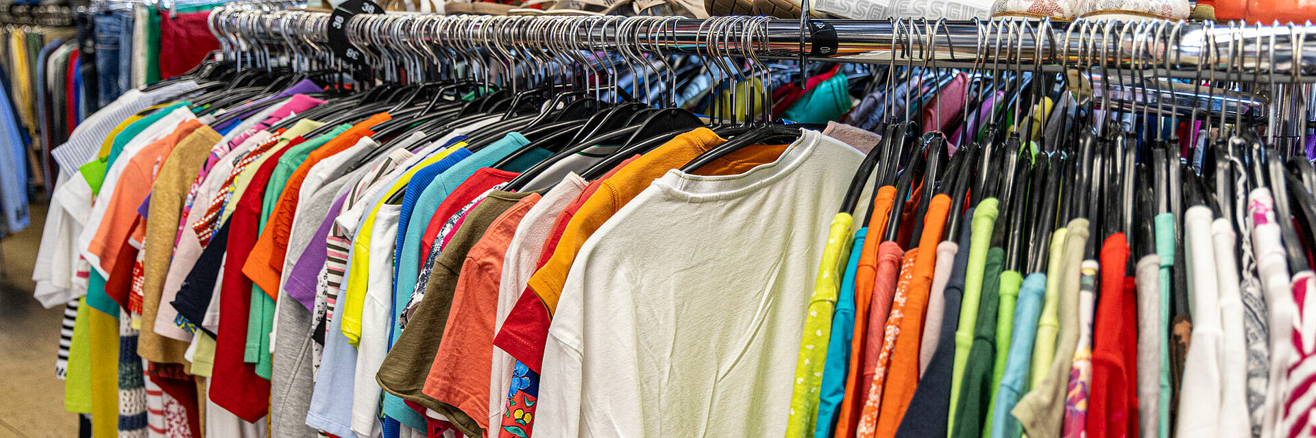 Bunte Auswahl an Secondhand-Mode im DRK Kleiderladen Gießen Kleiderstange mit bunten T-Shirts und Oberteilen im DRK Kleiderladen Gießen