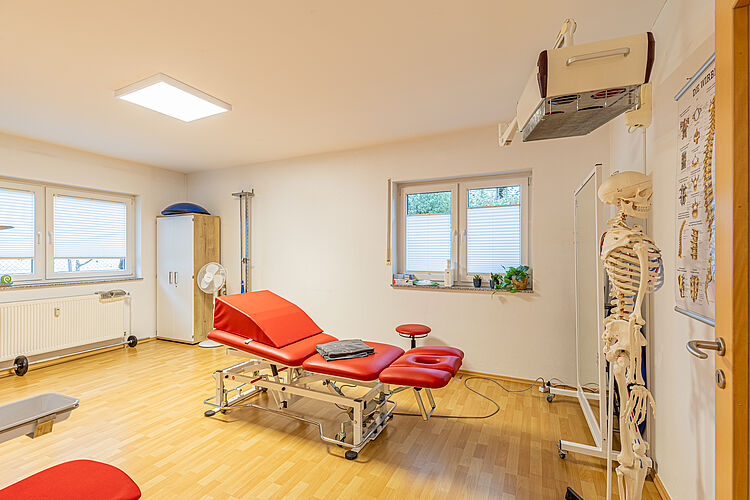 Behandlungsraum mit roter Liege – DRK Therapiepraxis Alten-Buseck Physiotherapieraum mit roter Therapieliege und Skelettmodell