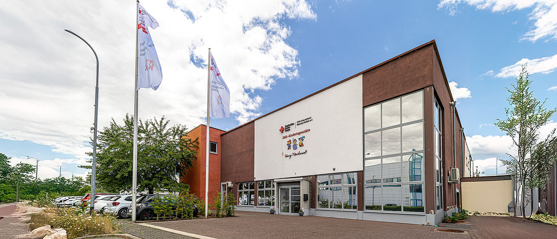 DRK-Kita „Henrys kleine Forscher“ in Staufenberg-Daubringen – Moderne Kindertagesstätte des DRK Mittelhessen Außenansicht der DRK-Kindertagesstätte „Henrys kleine Forscher“ in Staufenberg-Daubringen mit Fahnen und Eingangsbereich