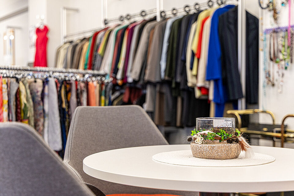 DRK Kleiderladen Lollar – Sitzecke mit Mode im Hintergrund Sitzecke im DRK Kleiderladen Lollar mit Kleiderständern im Hintergrund