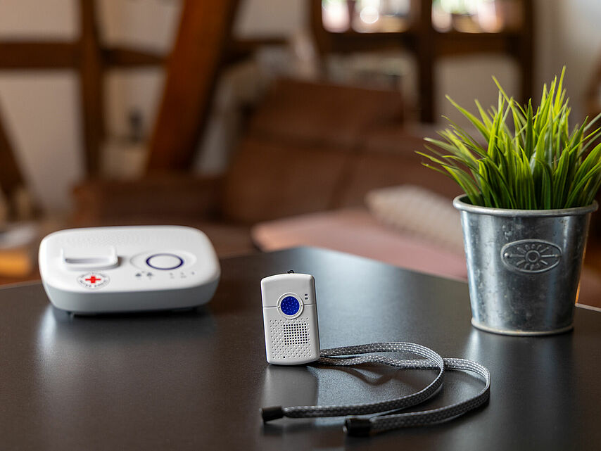DRK Hausnotruf – zuverlässige Hilfe auf Knopfdruck Hausnotrufgerät mit Notrufsender und rotem Kreuz auf einem Tisch